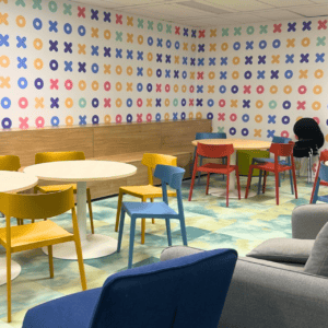 Salle de repos colorée moderne avec papier peint X et O, sièges variés et tables.