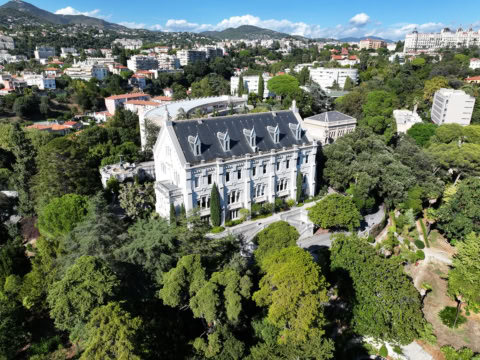 Manoir historique dans parc vu aérien, jardins formels, toits rouges et collines urbaines méditerranéennes.