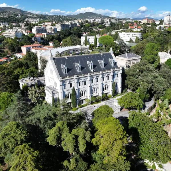 Manoir historique dans parc vu aérien, jardins formels, toits rouges et collines urbaines méditerranéennes.