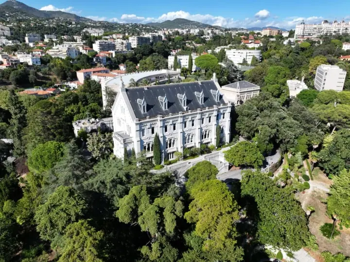 Manoir historique dans parc vu aérien, jardins formels, toits rouges et collines urbaines méditerranéennes.