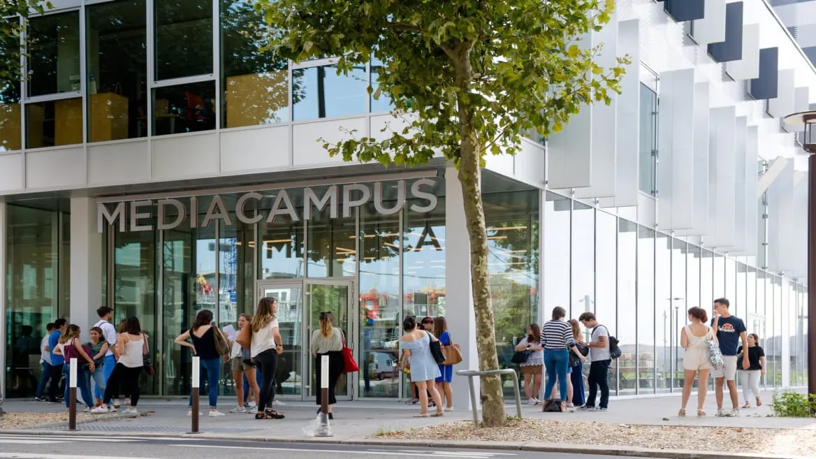 Entrée MediaCampus : jeunes étudiants devant bâtiment moderne à façade vitrée, campus urbain.