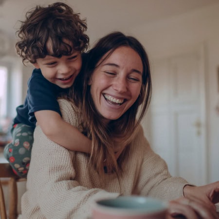 Mère riant avec enfant en portage près dun ordinateur portable à la maison.