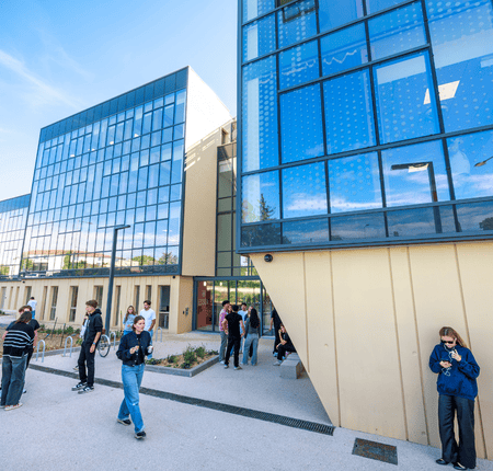 Cour extérieure moderne entre bâtiments en verre, façades réfléchissantes, personnes, architecture contemporaine ensoleillée.