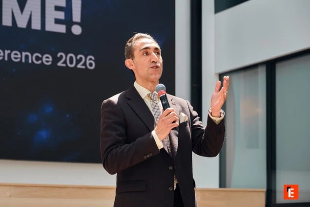 Orateur en costume au micro sur scène lors de la conférence 2026.
