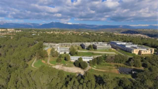 Panorama aérien dun campus avec bâtiments modernes, forêt et montagnes enneigées.