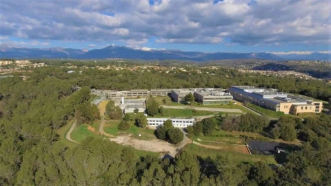 Panorama aérien dun campus avec bâtiments modernes, forêt et montagnes enneigées.