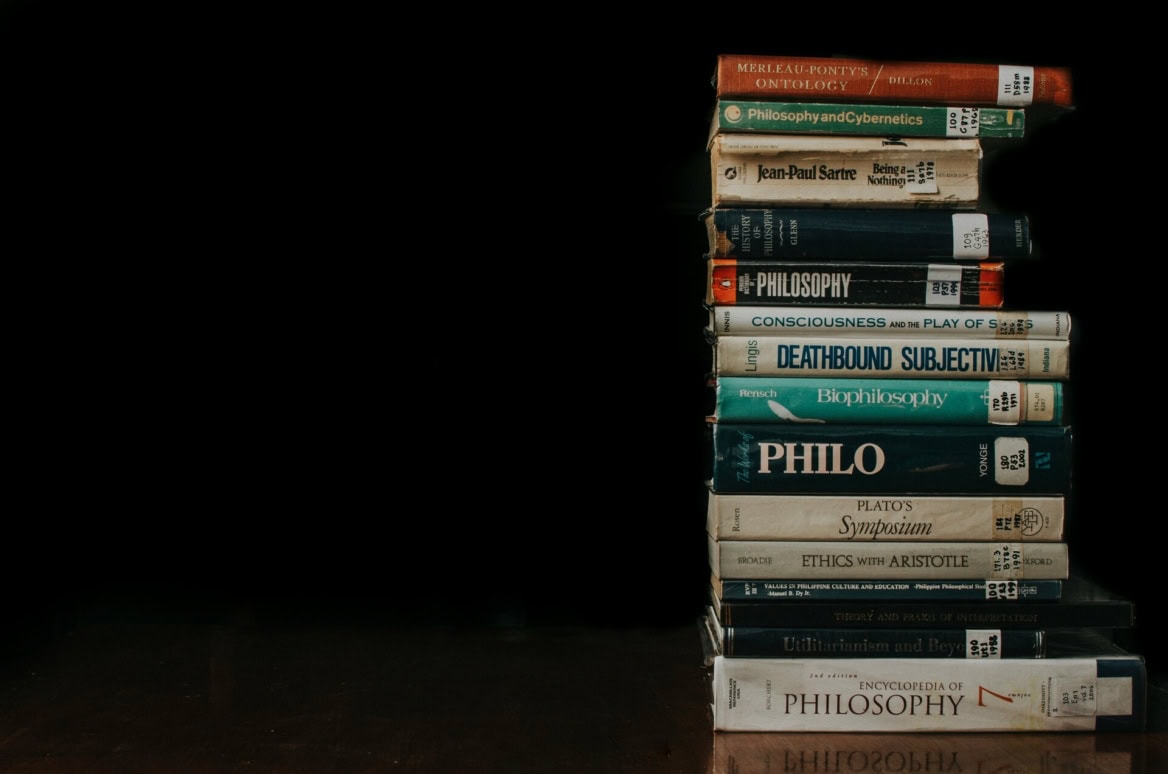 Pile de livres de philosophie (Sartre, Platon), usure et marques de bibliothèque, fond noir.