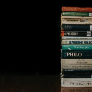 Pile de livres de philosophie (Sartre, Platon), usure et marques de bibliothèque, fond noir.