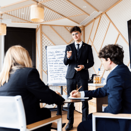 Présentation en réunion dentreprise : présentateur devant flipchart, équipe attentive dans salle moderne.