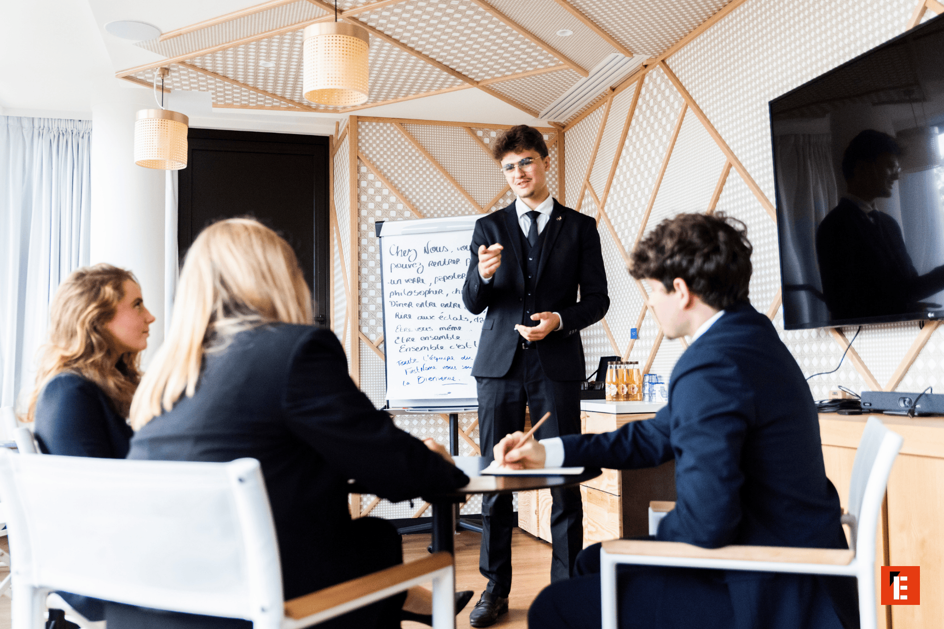 Présentation en réunion dentreprise : présentateur devant flipchart, équipe attentive dans salle moderne.