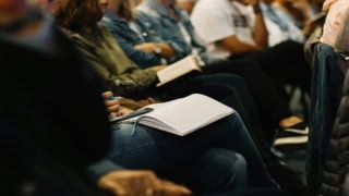 Prise de notes au séminaire : participant avec carnet, stylo et smartphone.