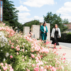 Promenade de femmes sur chemin fleuri sous ciel bleu, fleurs roses au premier plan.