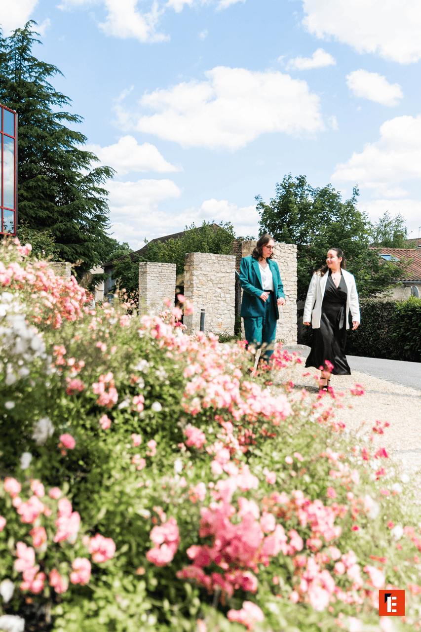 Promenade de femmes sur chemin fleuri sous ciel bleu, fleurs roses au premier plan.