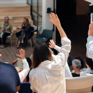 Public en atelier intérieur, audience aux mains levées, intervenants sur scène.