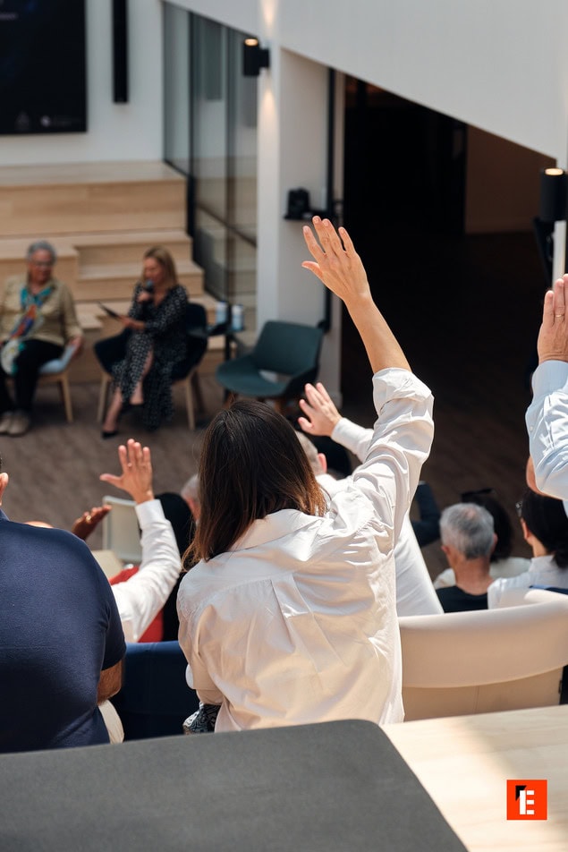 Public en atelier intérieur, audience aux mains levées, intervenants sur scène.