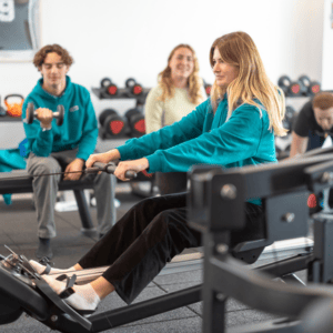 Femme rameuse sur rameur en salle de sport, entraînement collectif, haltères et kettlebells.