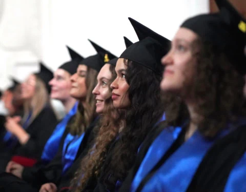 Étudiants en toges noires et écharpes bleues alignés lors dune remise de diplômes.