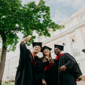 Trois diplômés en toge prennent un selfie lors dune remise de diplôme.