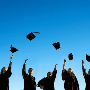 Remise de diplômes : étudiants en toge lançant leurs toques vers un ciel bleu.