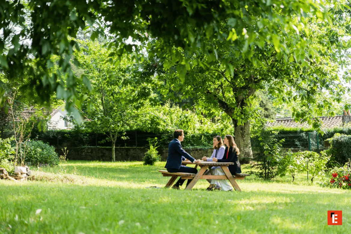 Réunion informelle dans un jardin sous un arbre, trois personnes autour dune table pique-nique.