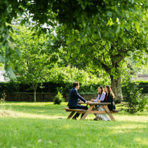 Réunion informelle dans un jardin sous un arbre, trois personnes autour dune table pique-nique.