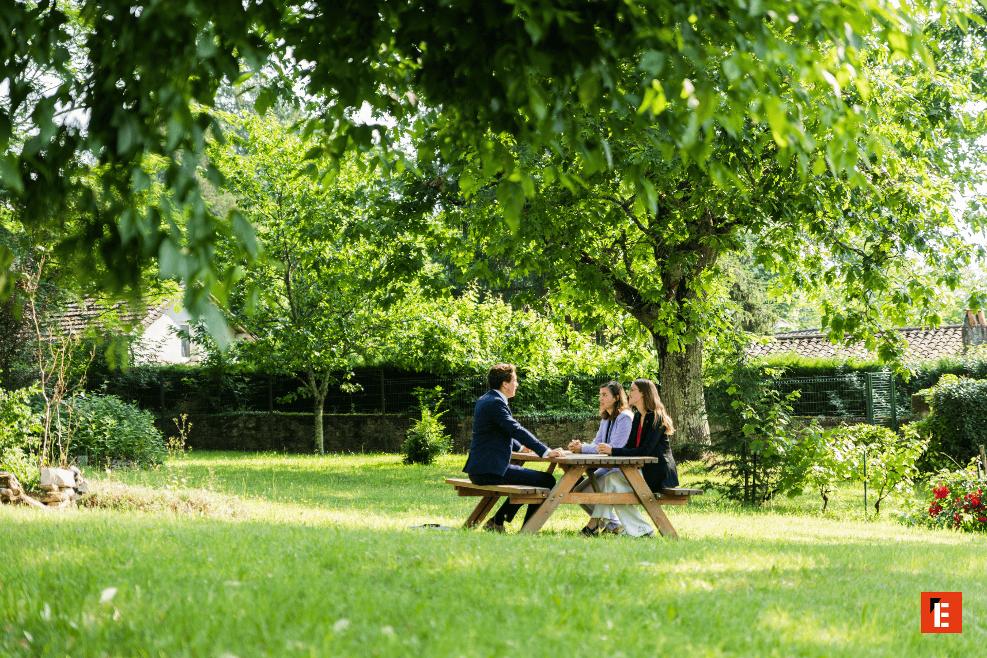 Réunion informelle dans un jardin sous un arbre, trois personnes autour dune table pique-nique.
