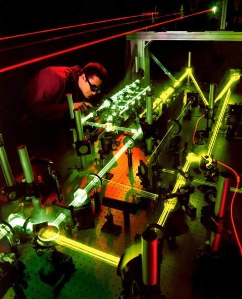Table optique de laboratoire avec lasers verts et rouges, montures et technicien.