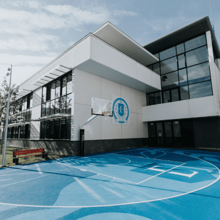 Court de basket bleu devant bâtiment scolaire moderne à façade blanche vitrée.