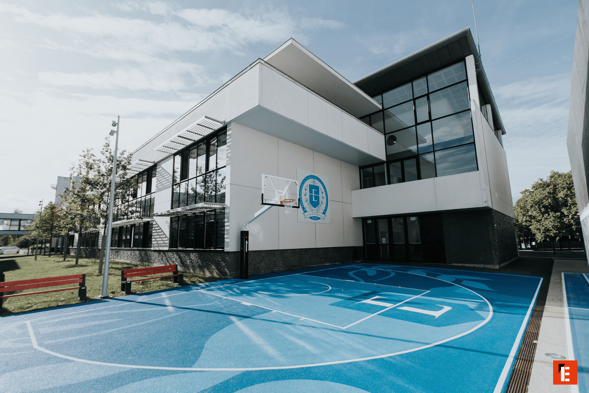 Court de basket bleu devant bâtiment scolaire moderne à façade blanche vitrée.