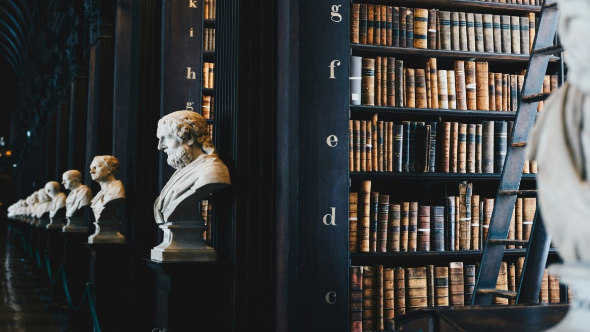 Bibliothèque ancienne avec rangée de bustes en marbre et rayonnages de livres anciens.