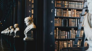 Bibliothèque ancienne avec rangée de bustes en marbre et rayonnages de livres anciens.