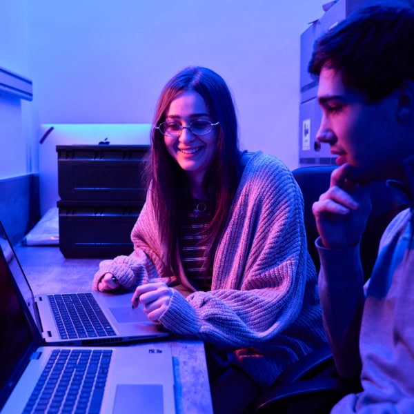 Étudiants CAMPUS ESGI collaborant sur ordinateurs portables sous éclairage néon dans laboratoire.