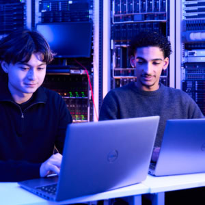Étudiants ESGI avec laptops devant racks de serveurs, laboratoire réseaux et cybersécurité.