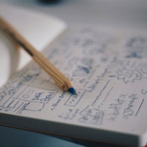 Carnet de croquis ouvert avec crayon posé, notes manuscrites et esquisses rapides.