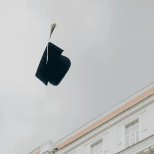 Chapeau de diplômé noir avec gland doré lancé dans le ciel au-dessus dun bâtiment classique.