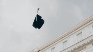 Chapeau de diplômé noir avec gland doré lancé dans le ciel au-dessus dun bâtiment classique.