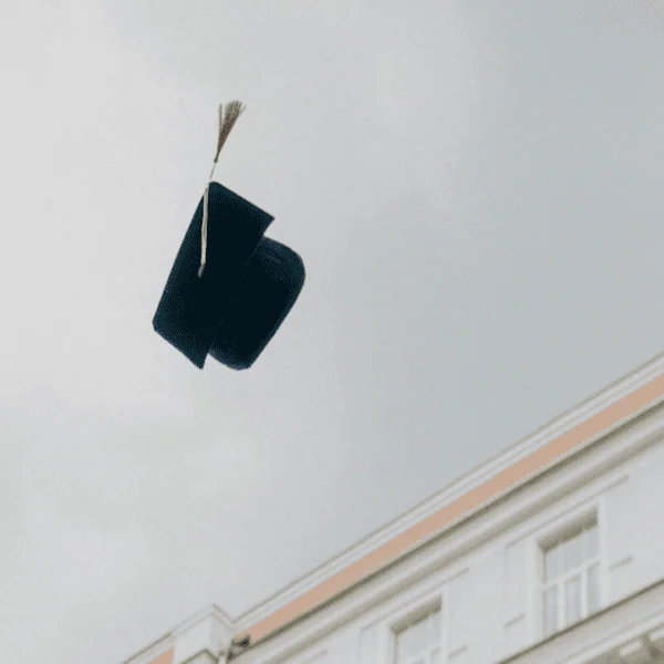 Chapeau de diplômé noir avec gland doré lancé dans le ciel au-dessus dun bâtiment classique.