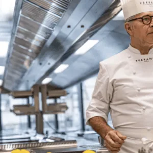 Chef en toque et veste blanche dans cuisine professionnelle industrielle, citrons sur plan de travail.