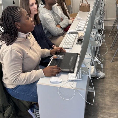 Classe informatique avec quatre étudiants concentrés sur des iMacs, travail collaboratif.