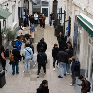 Cour intérieure de campus avec étudiants discutant près dune table et portes en briques.