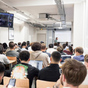 Cours atelier informatique en amphithéâtre avec étudiants, ordinateurs portables et projection.