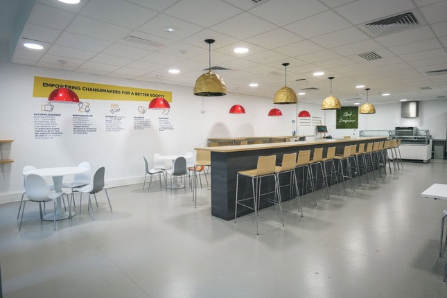 Cuisine commune moderne avec grande table centrale, tabourets, kitchenette et lampes design.