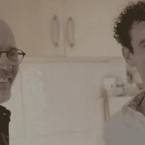 Portrait de deux hommes souriants dans une cuisine chaleureuse, photo intime et décontractée.