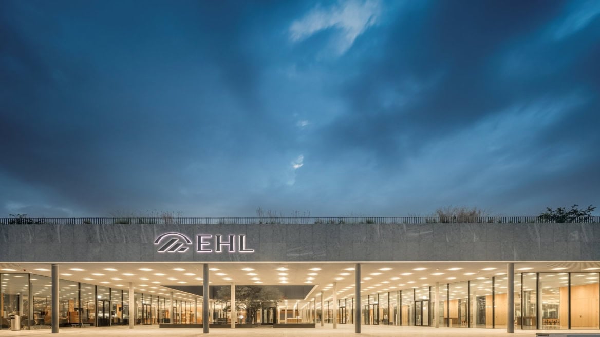 Entrée du bâtiment moderne EHL en verre, éclairage chaleureux au crépuscule.