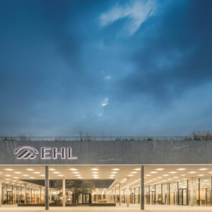 Entrée du bâtiment moderne EHL en verre, éclairage chaleureux au crépuscule.