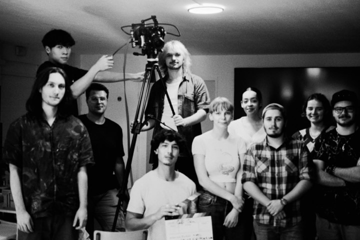 Équipe de tournage autour dune caméra sur trépied avec clap, photo noir et blanc.