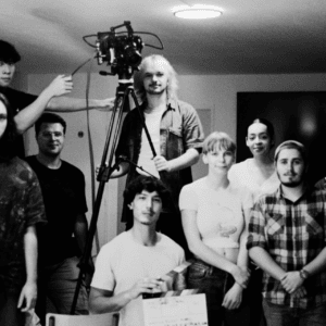Équipe de tournage en studio noir et blanc avec caméra professionnelle, trépied et clap.
