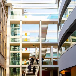 Atrium lumineux ESCP Business School avec escalier central, verrière, mur en brique et façade vitrée.