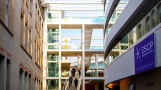Atrium lumineux ESCP Business School avec escalier central, verrière, mur en brique et façade vitrée.