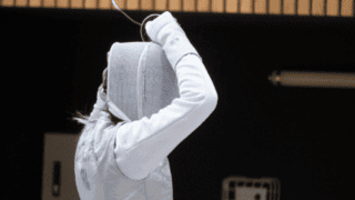 Athlète descrime ajustant son masque, dos vêtu de lamé et gant blanc.